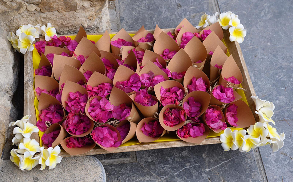 eco-friendly confetti cones with bright pink bougainvillae confetti, lying on a wooden tray, layered in yellow paper and wjite and yellow latex plumeria in the corners - sustainable luxury wedding