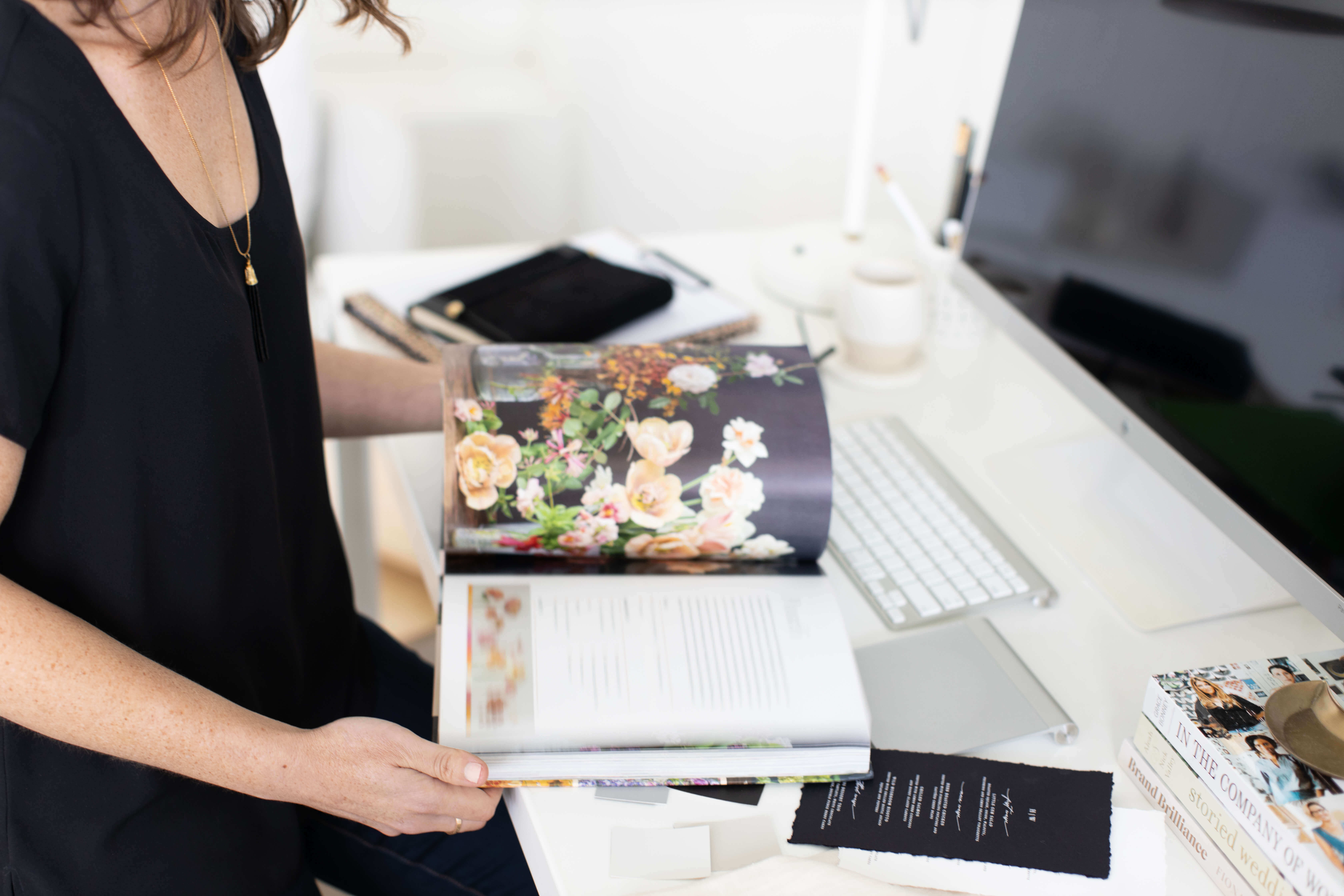 a lady with a black top reading wedding magazines in front of a laptop