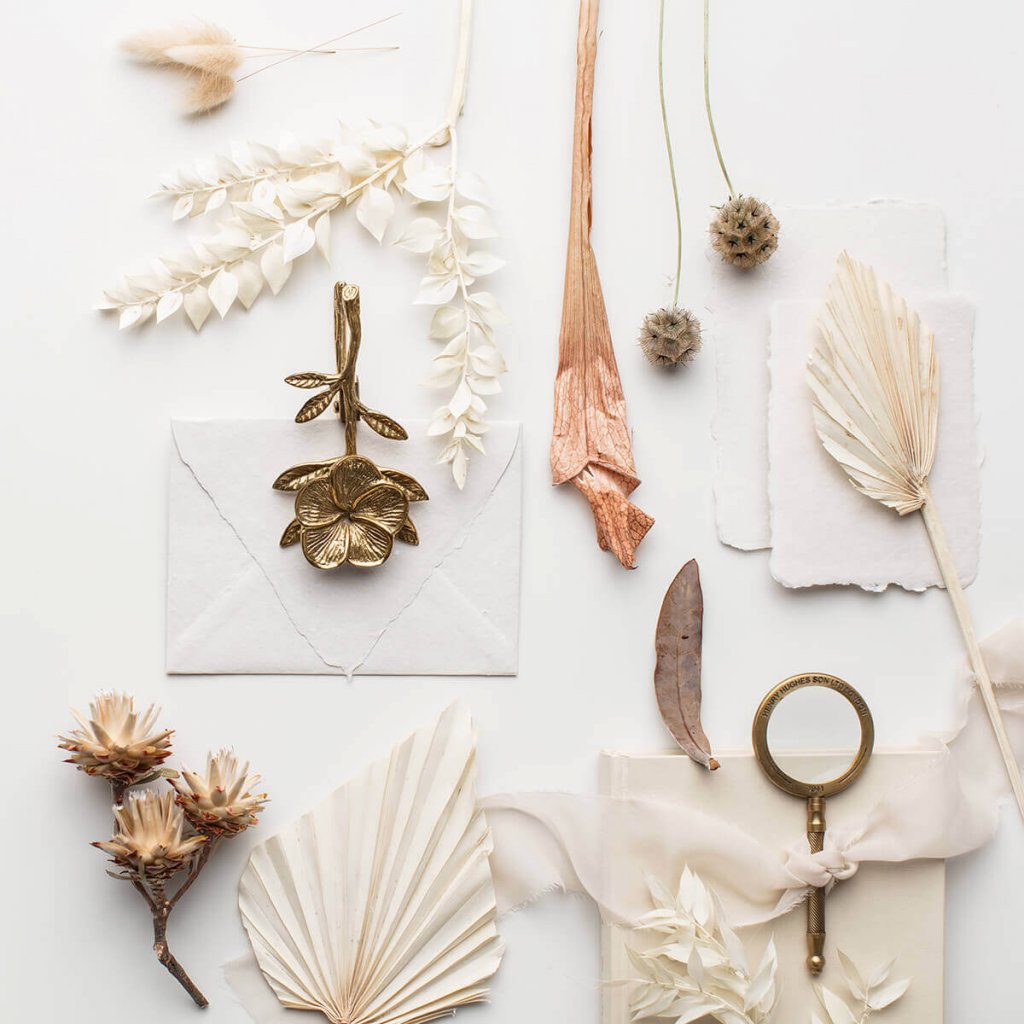 environmentally friendly wedding invitations featuring cream paper, white envelopes, some brass paper cutter and flower ornament, cream dry palm leaves, dry wild cream and rust flowers, a cream ribbon, dired rusty leaves and some cream bunny tails - sustainable luxury wedding