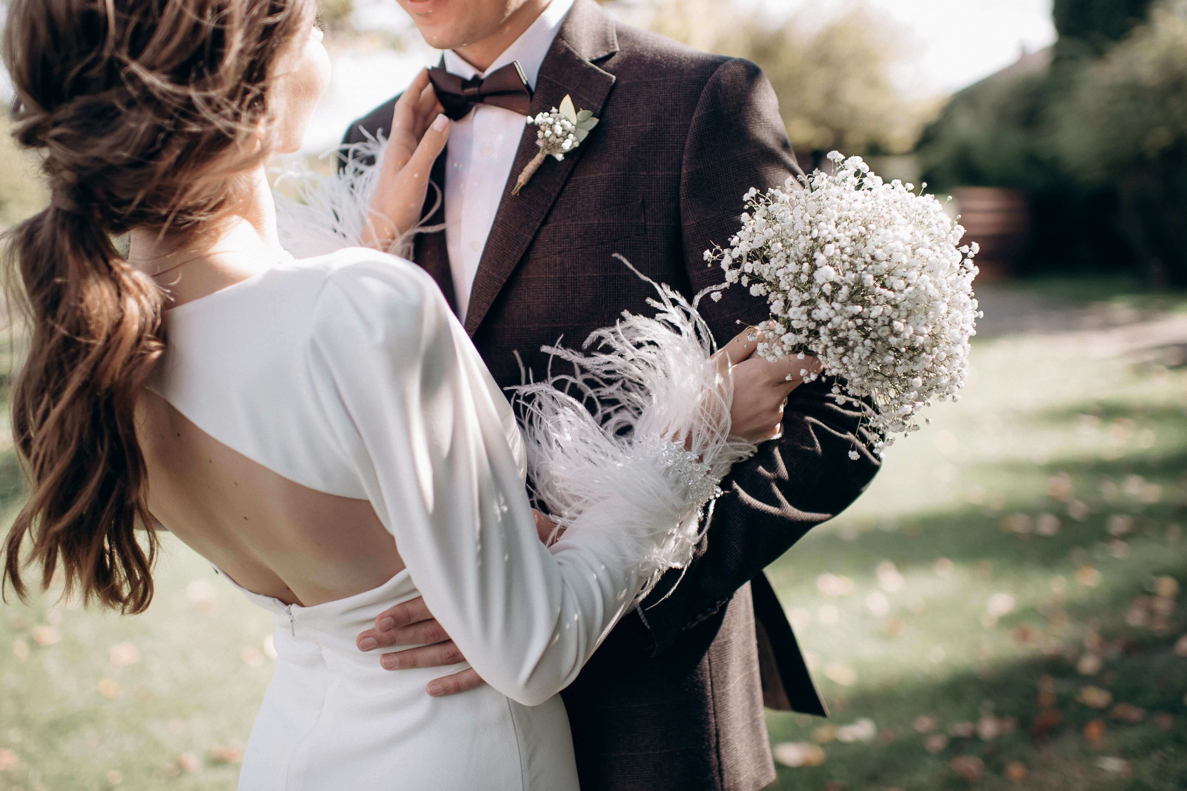 newlywed couple. brunette bride with low ponytail, open back dress holding a baby's breath bouquet and resting her hande on groom wearing a black tux, bow tie and babys breath buttonhole