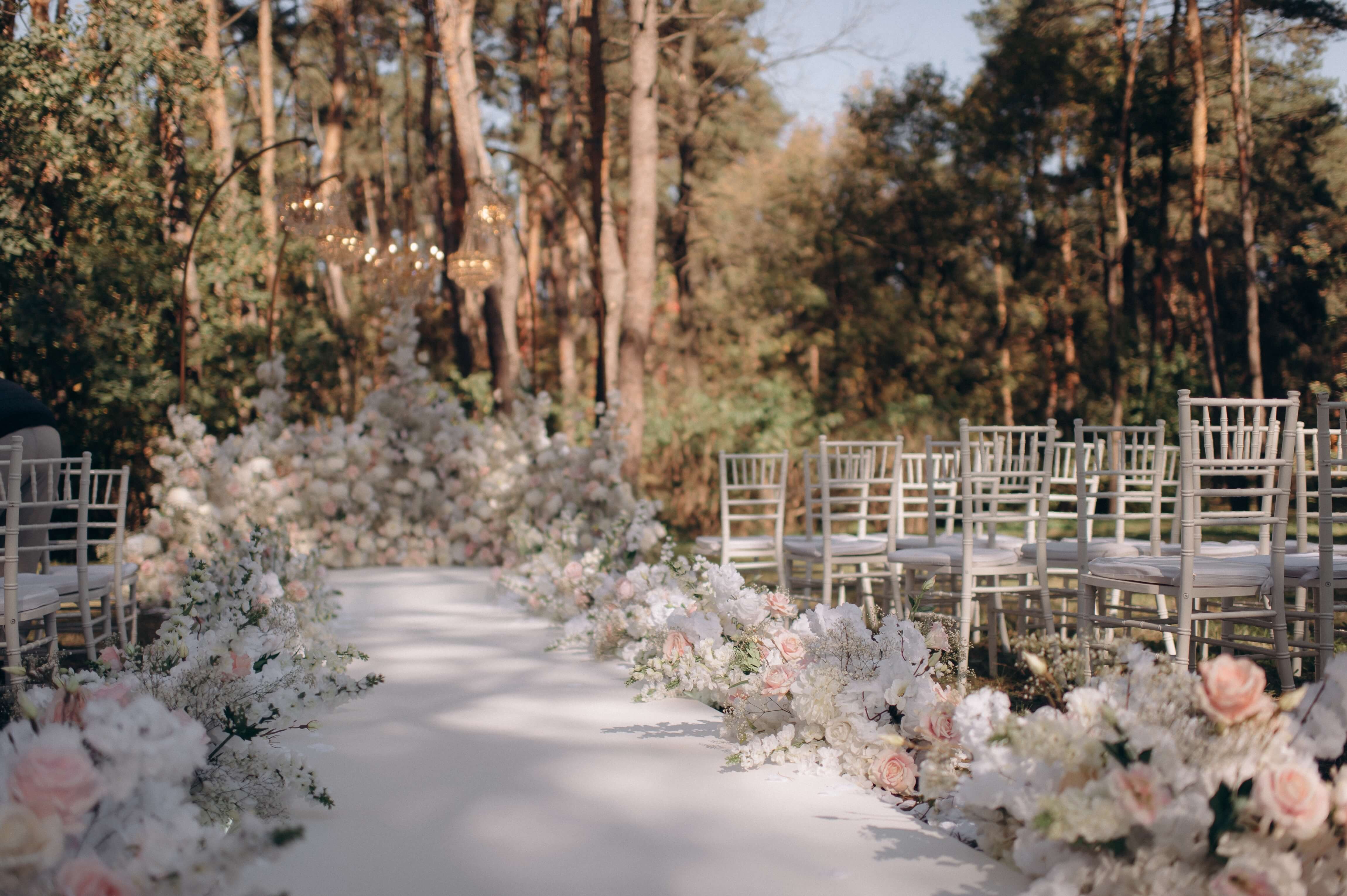 enchanted forest wedding ceremony with white chairs and aisle and pink and white florals