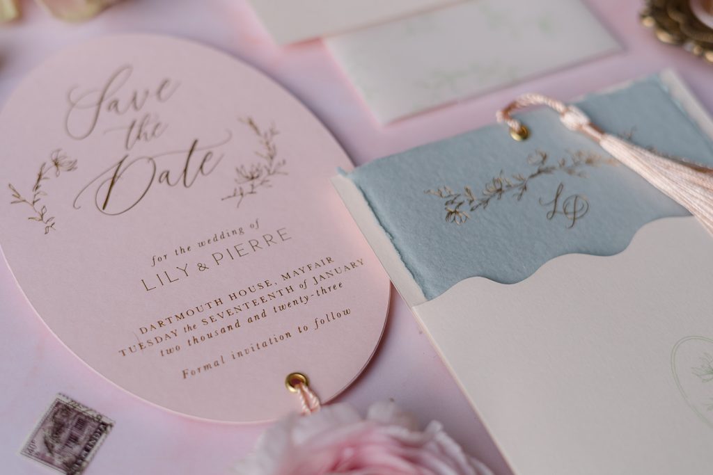 close-up of a flatlay Pink save the dates, jade wedding invite and cream envelopes Stationary suite with gold foil letterpress writing on a pink backdrop