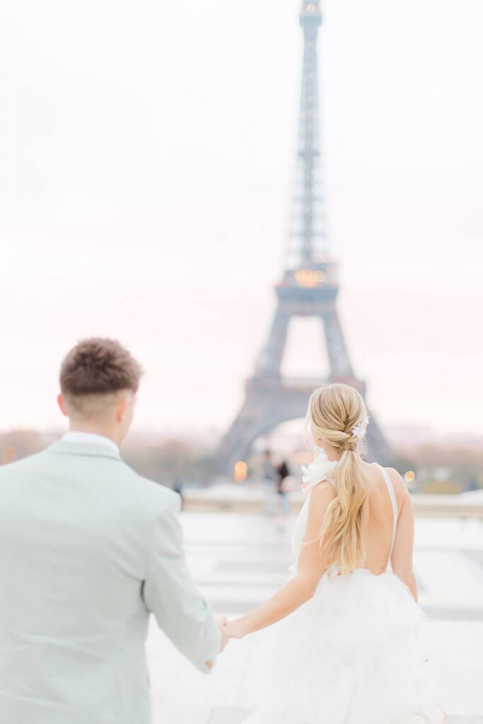 Groom and bride walking towards the Eiffel Tower holding hands