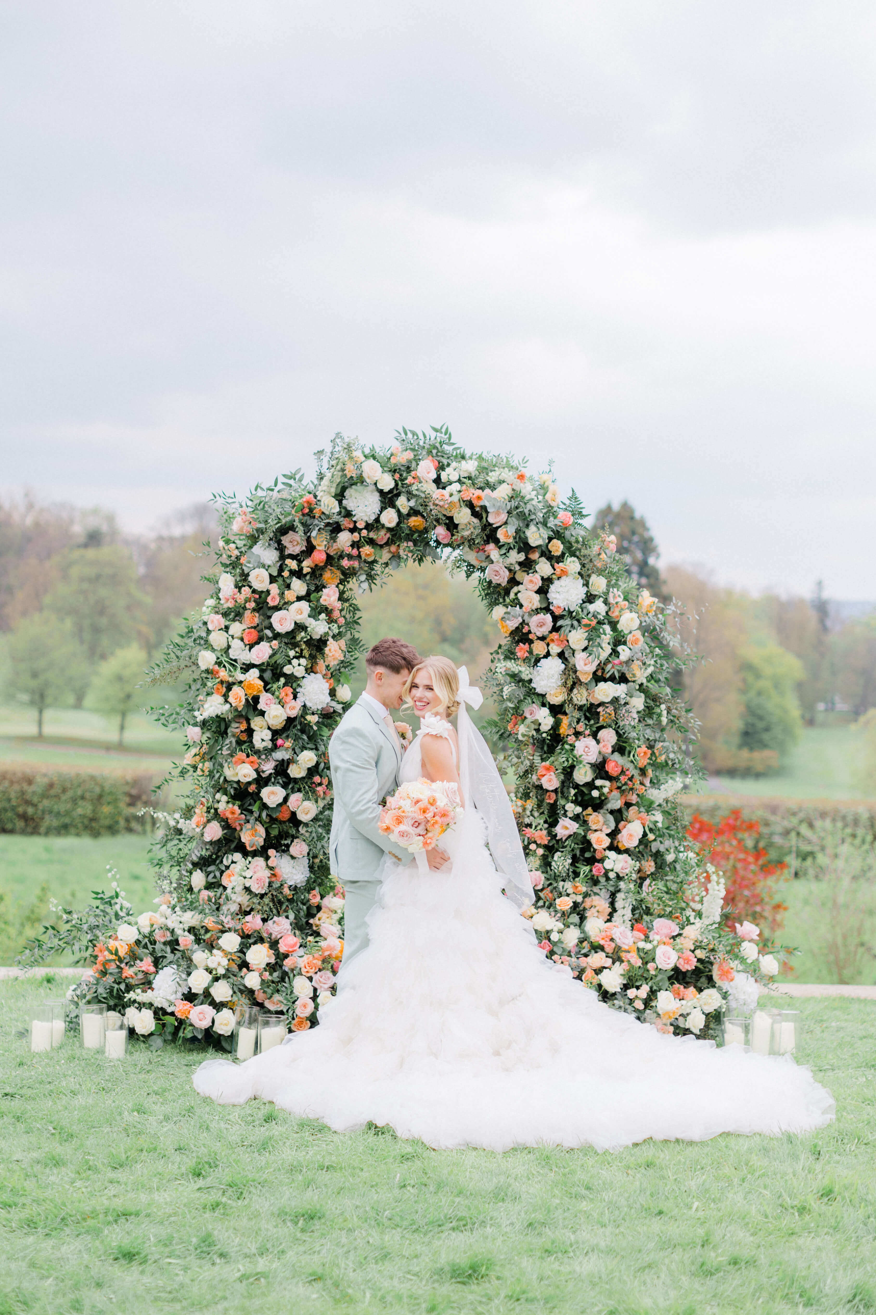 bride and groom standing in front Paris Wedding Chateau garden wedding ceremony set up with Pastel Floral arch on a lawn in front of Chateau Bouffemont