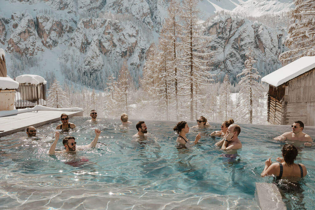 wedding guests welcome party in heated pool with snowy mountain in the background