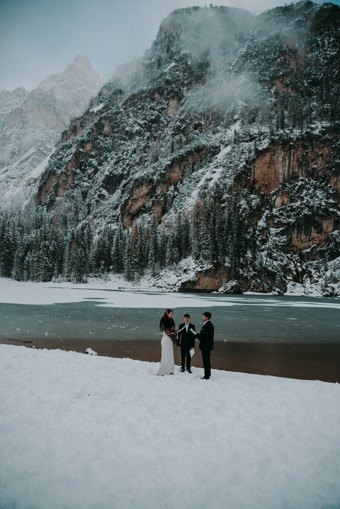  bride and groom looking at ceach other holding hands  and celebrant behind them at a snowy lake ceremony