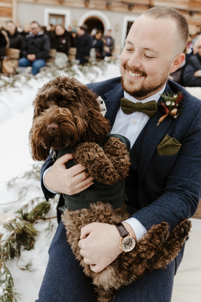 best. man smiling  hugging groom dog at winter wedding ceremony on the snow