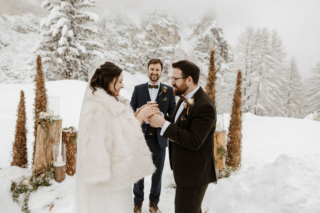 newlywed bride and groom holding a cup at winter wedding ceremony on the snow