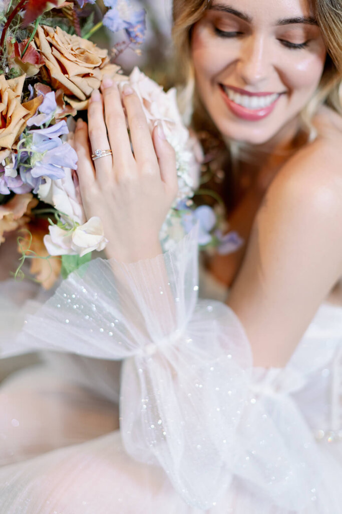 blonde bride's close up of wedding and engagement ring while gently holding her bouquet with lilac, toffee and cream flowers