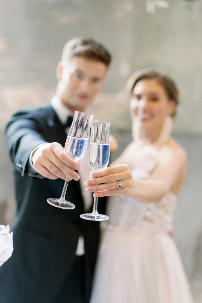close up of 2 flutes held by newly wed couple toasting , their look blurred and the flutes are on focus