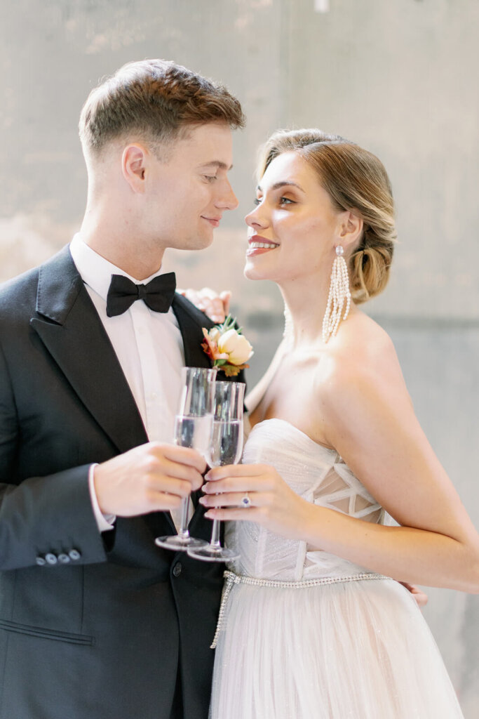 portrait of newly wed couple toasting with flutes looking into each other eyes, she's tilting her head slightly