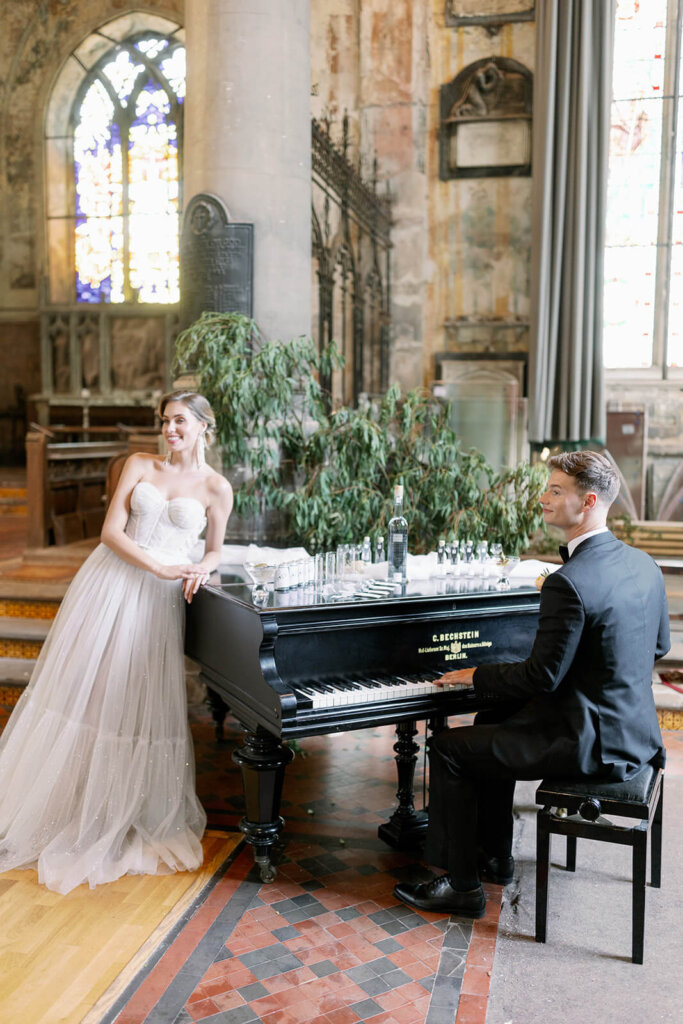 bride and groom captured by a black piano. he's playing and she's leaning on the piano side