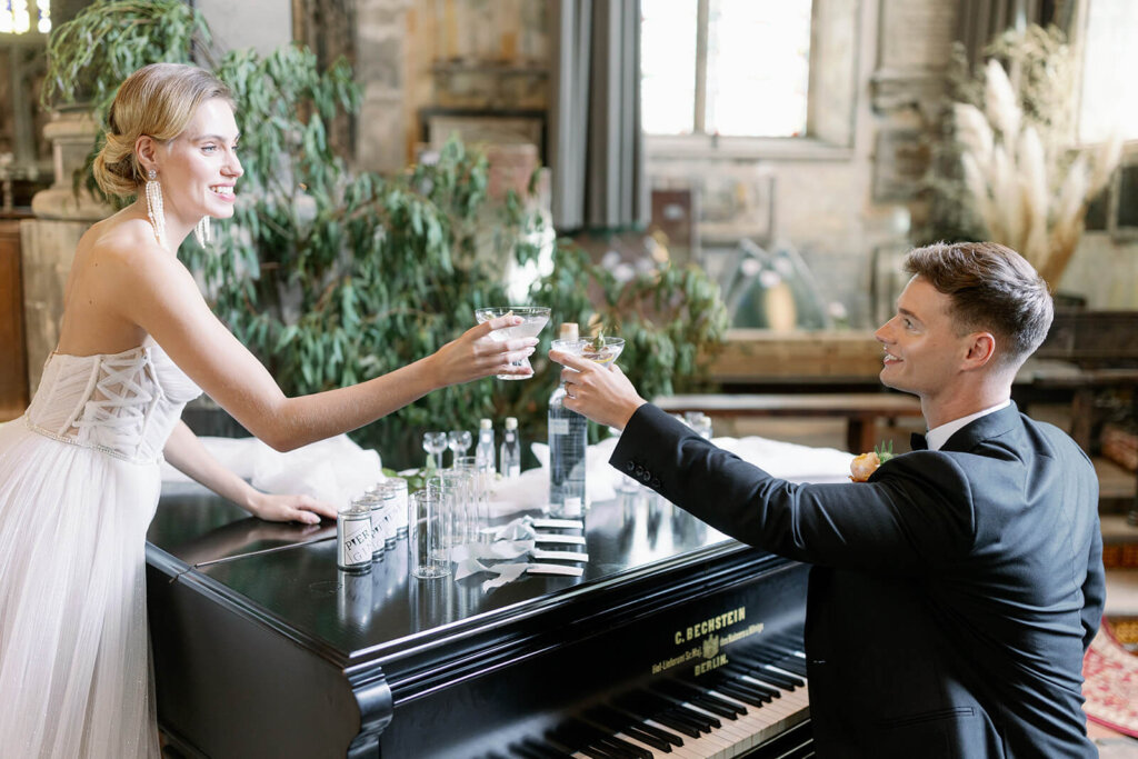 hands of bride and groom toasting with a signature cocktails with dry orange slice decoration over a black piano