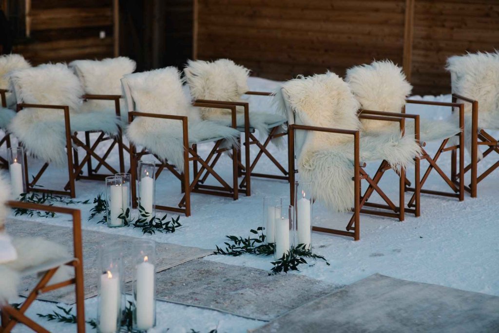 outdoors wedding ceremony chiars with faux fur chairs , candles down the snowy aisle 