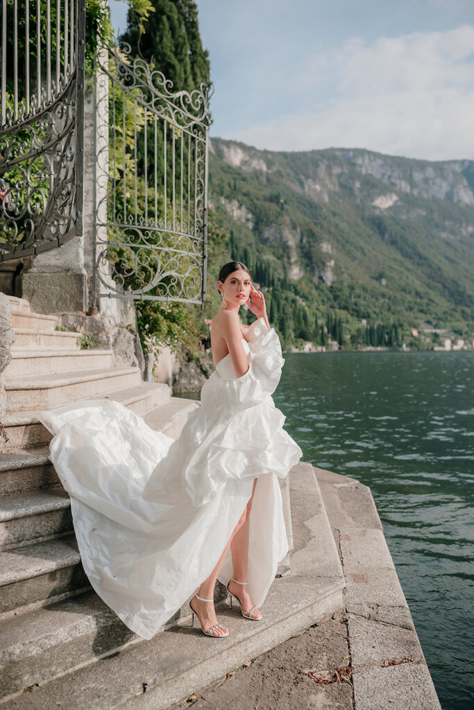 Villa Cipressi gate to pier with bride posing with lake and other villas in the background- Lake Como wedding planner