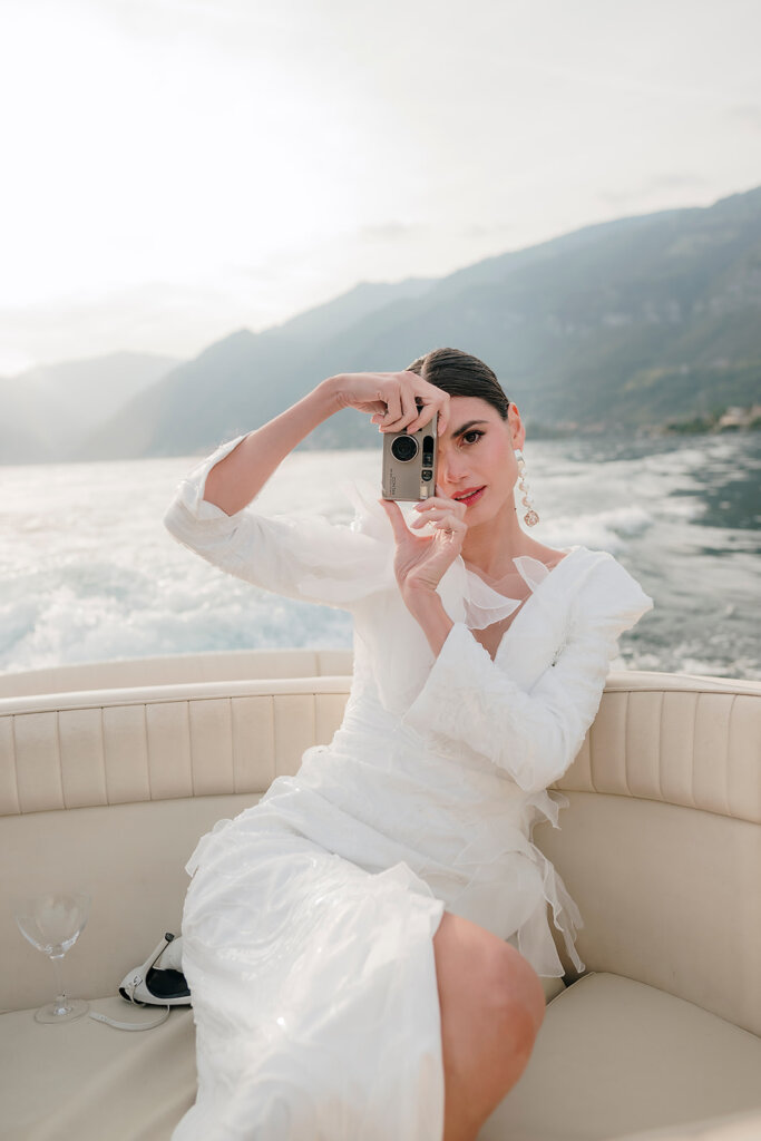 bride on boat departing from Villa Cipressi  pretending to take pictures f the photographer- Lake Como wedding planner 